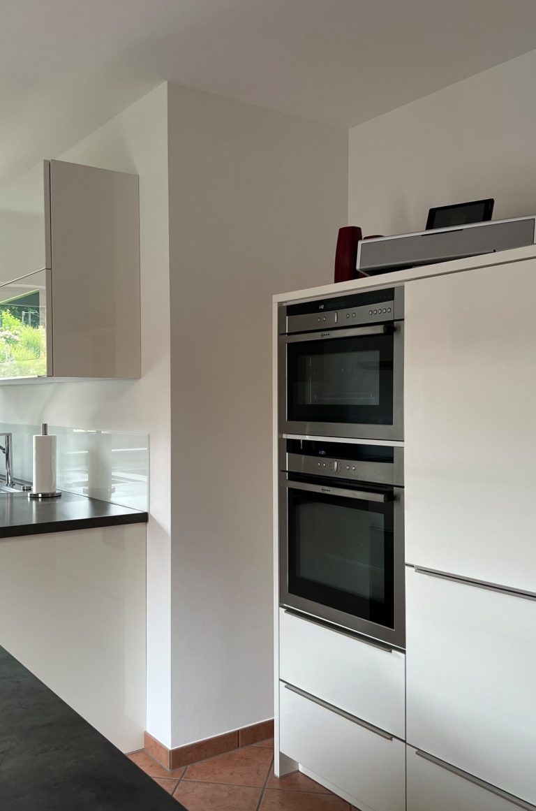 Apartment 2, Küche Helle Küche mit weißen Möbeln, Herd, Kühlschrank und Wanduhr.