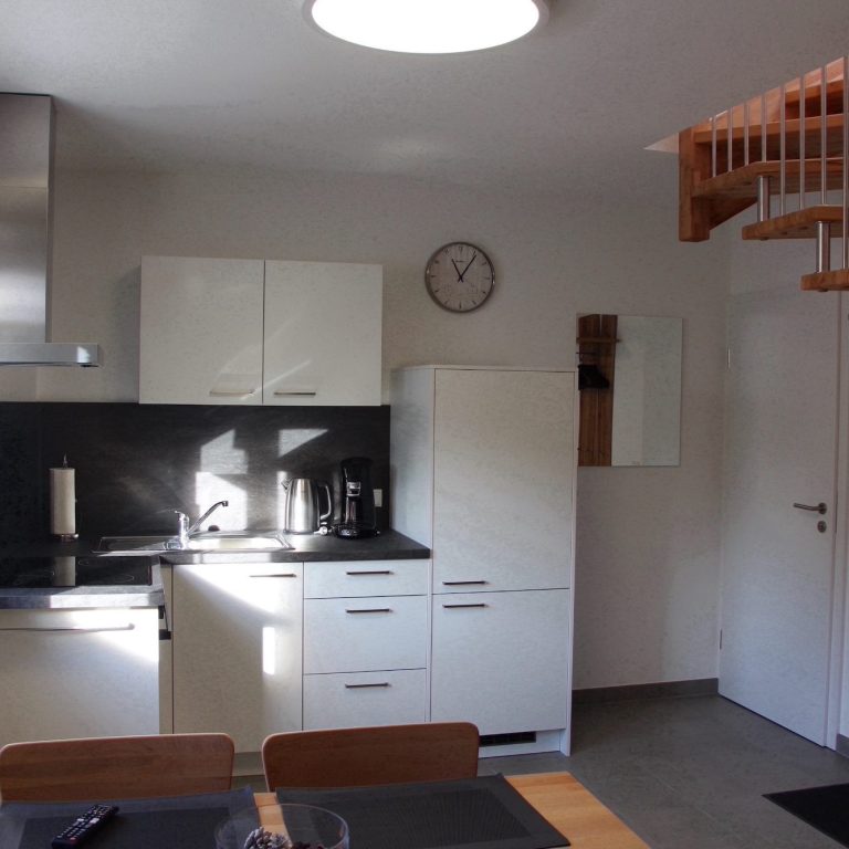 Apartment 2, Schlafzimmer Ein Bett mit weißen Kissen, Nachttisch und Leuchte in einem hellen Raum.